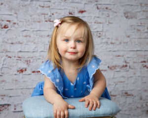 Baby Milestone Portrait of a Cute toddler aged girl wearing a blue dress and leaning on a blue stool