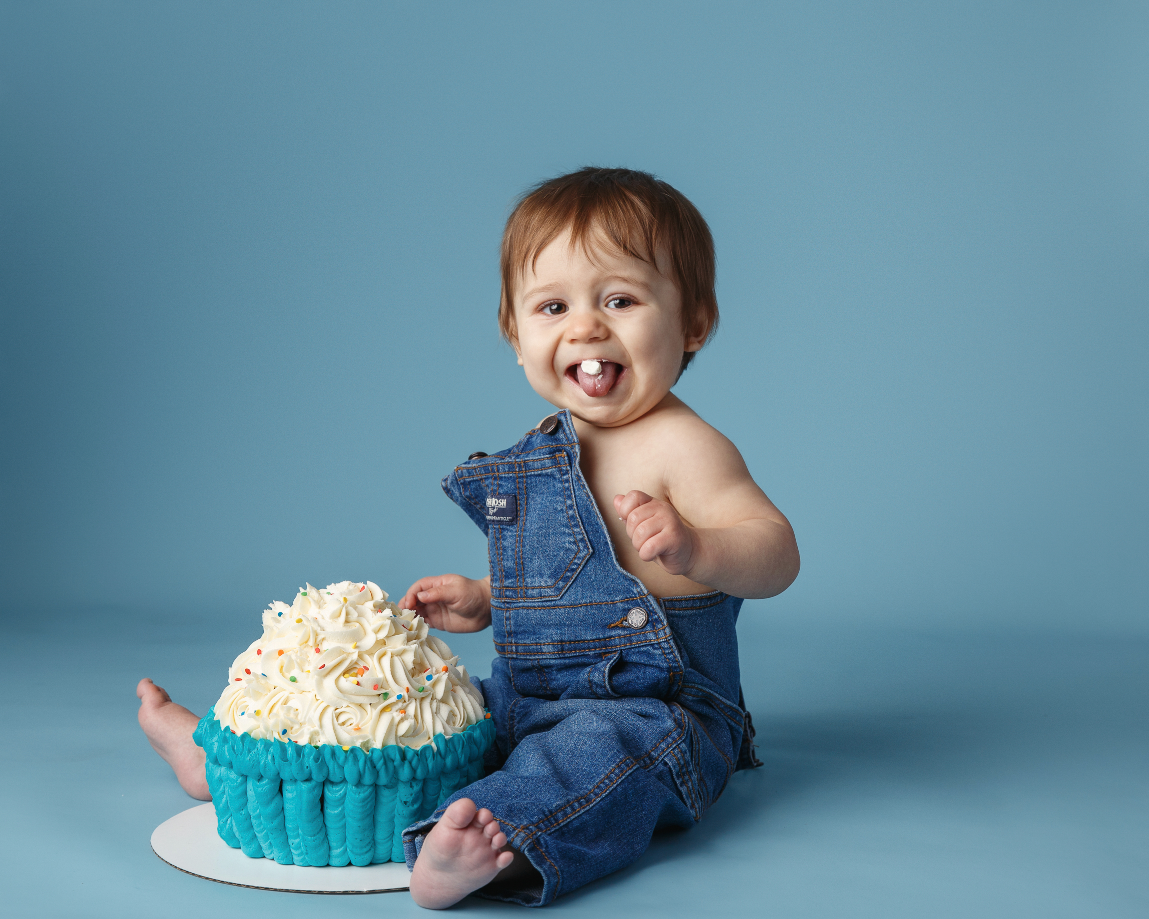 Photo of a first birthday cake smash session with one year old wearing overalls