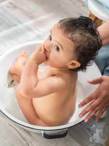 Photo of a one year old sitting in a tub and getting a bath after his first birthday cake smash session
