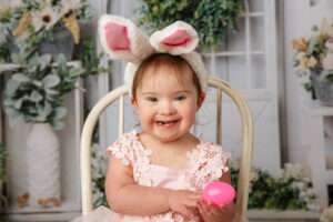 Little girl sitting on a chair wearing bunny ears for an Easter mini session