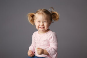 Cute little girl with blond hair and pig tails wearing a pink shirt and smiling