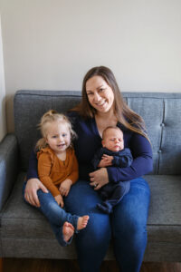 Mom sitting on a couch and introducing the new baby to it's older sibling