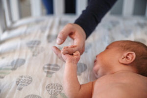 Newborn in his crib with mom holding his little hand