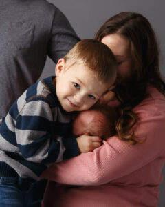 A happy big brother hugging his new brother as he lays in his mothers arms