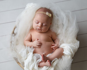 Portrait of a Newborn Baby girl with a pink headband laying on a white blanket