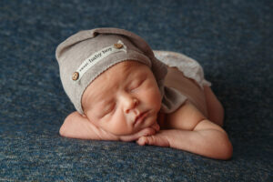 Newborn photoshoot image of a baby laying on its tummy wearing a sleep cap