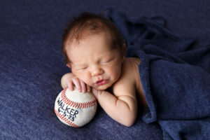 Portrait of a newborn baby boy resting his hands and chin on a base ball