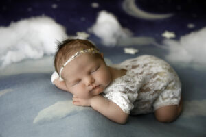 Little baby girl during a newborn photoshoot posed on a blue blanket with clouds and moon background