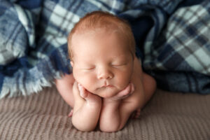 Portrait of a newborn baby with a plaid blanket posed with his hands under his chin