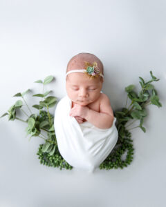 Cute baby girl wrapped in white with eucalyptus branches