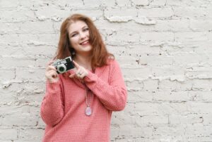 Photo of a woman photographer wearing a pink sweater and holding a camera.