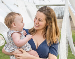Motherhood Portrait of a mom with her baby daughter outside in front of a clothesline with sheets blowing in the wind.