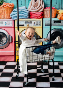 Image of a two-year-old girl sitting in a laundromat basket and being silly during a mom and me photo session