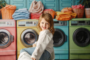 Cute four-year-old girl standing in front of a colorful background with washing machines and folded towels
