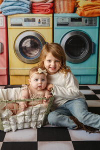 Two sisters sitting on the floor of a laundromat themed background 