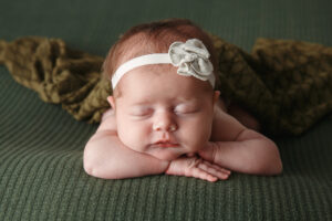 Clost up newborn photos of a baby girl wearing a cute headband and sleeping on a green blanket