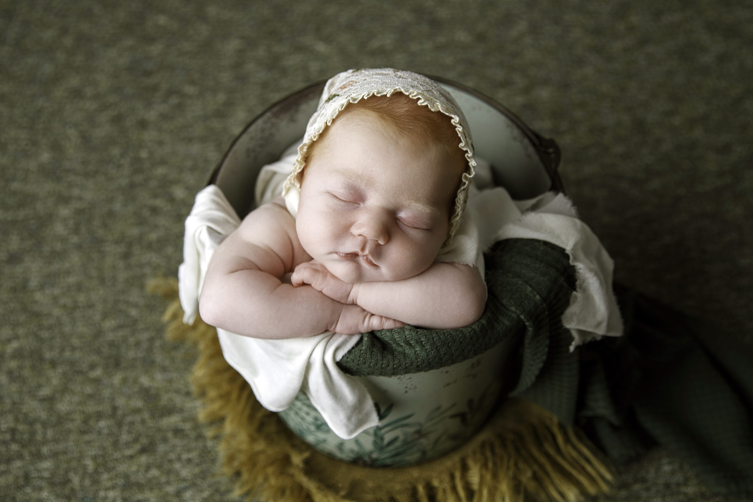 Newborn Photos of a baby girl wearing a bonnet and sleeping in a bucket