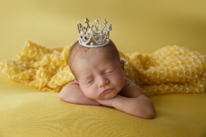 Newborn Photos of a baby girl wearing a crown on her head and laying on a yellow blanket