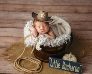 Cowboy themed Newborn Photo of a baby wearing a cowboy hat, sitting inside a bucket with a robe.