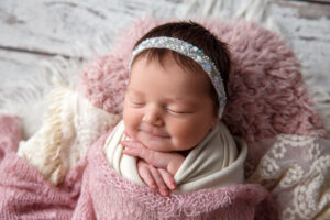 Portrait of a baby girl wrapped in a pink blanket with a little smile showing her cute newborn's personality.