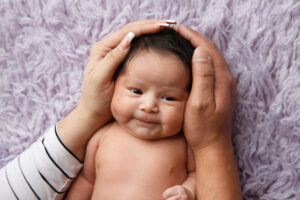 Image of a cute Newborn's personality with mom's hands encircling her head.