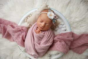 Newborn Baby Girl wrapped in a pink blanket laying in a basket on white background