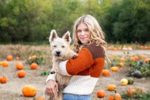 Teenage girl in a pumpkin patch using her dog as a prop for her senior portraits