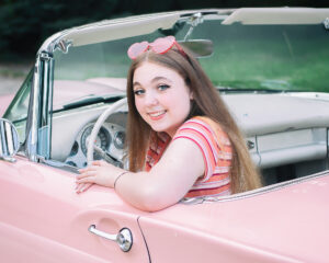 Senior girl with pink sunglasses using a prink classic Thunderbird convertable as a photo prop.