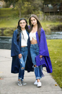 Two high school senior girls wearing cap and gowns for senior portrait session