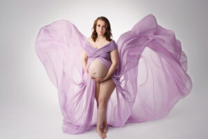 Pregnant woman wearing a purple flowing gown during a maternity photo session.