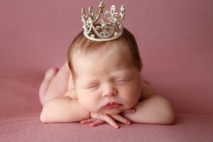 sleeping baby girl wearing a crown on a pink background