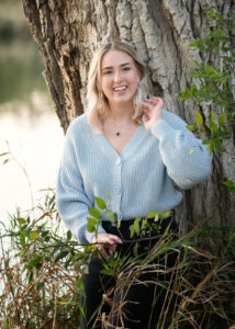 Smiling high school senior photographed near a tree by the river. 