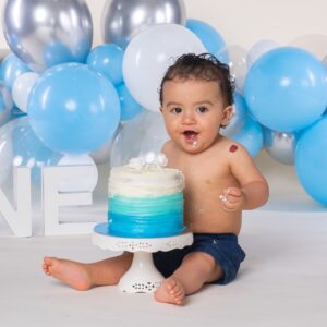 Little one year old boy with a birthday party cake and balloons.