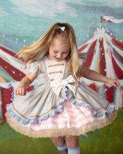 Preety 4 year old girl twirling in her birthday party dress with a circus tent behind her. 