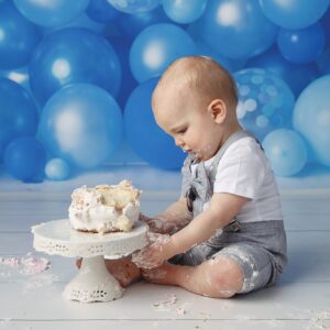 One year old baby boy celebrating his birthday with a cake smash and balloon background.