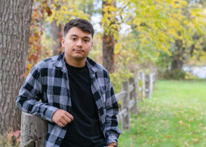 High school senior portrait of a boy in a flannel shirt standing near a split rail fence at Beckman Mills.