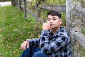 Senior boy sitting by a split rail fence at Beckman Mills in Beloit.