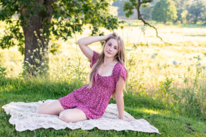 High school senior girl in a red dress on a blanket at a favorite senior picture location in Brodhead.