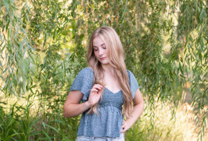 High school senior girl in a blue top near a weeping willow on the path a three rivers reserve.