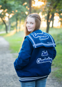 High school senior girl in lettermans jacket on a path at magnolia Bluffs in Evansville.