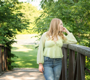 High school senior girl in a yellow blouse near a foot bridge at Palmer Park.