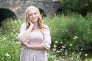 Portrait of a high school senior girl near a bridge with wildflowers in Janesville.