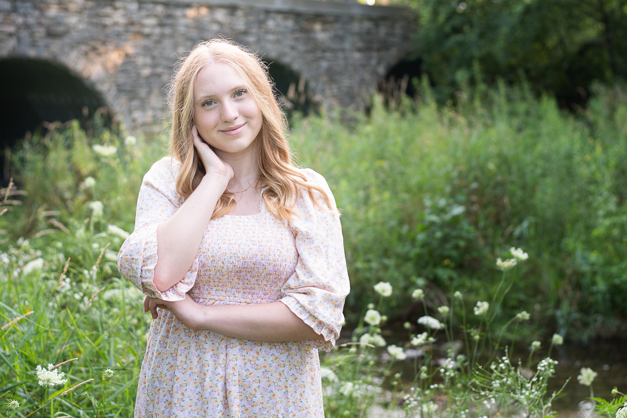 Portrait of a high school senior girl near a bridge with wildflowers in Janesville.