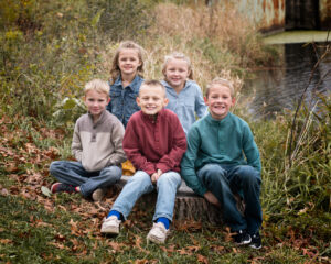 Group of five siblings for a family photo session outdoors near a pond.