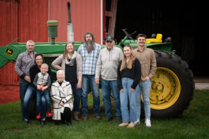 Large family photo at the farm outside a barn in front of the tractor.