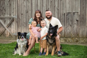 Family portrait of mom, dad, baby girl and big brother with two dogs outdoors.