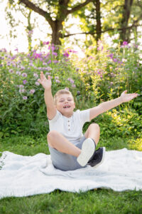 Seven year old boy sitting on a blanket and being silly for pictures.