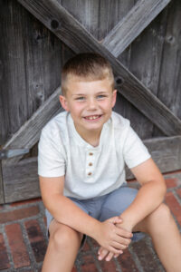 Portrait of a seven year old boy wearing a white shirt and sitting in front of a barn door.