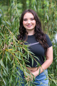 High school senior girl posing inside the branches of a weeping willow for her senior portraits.