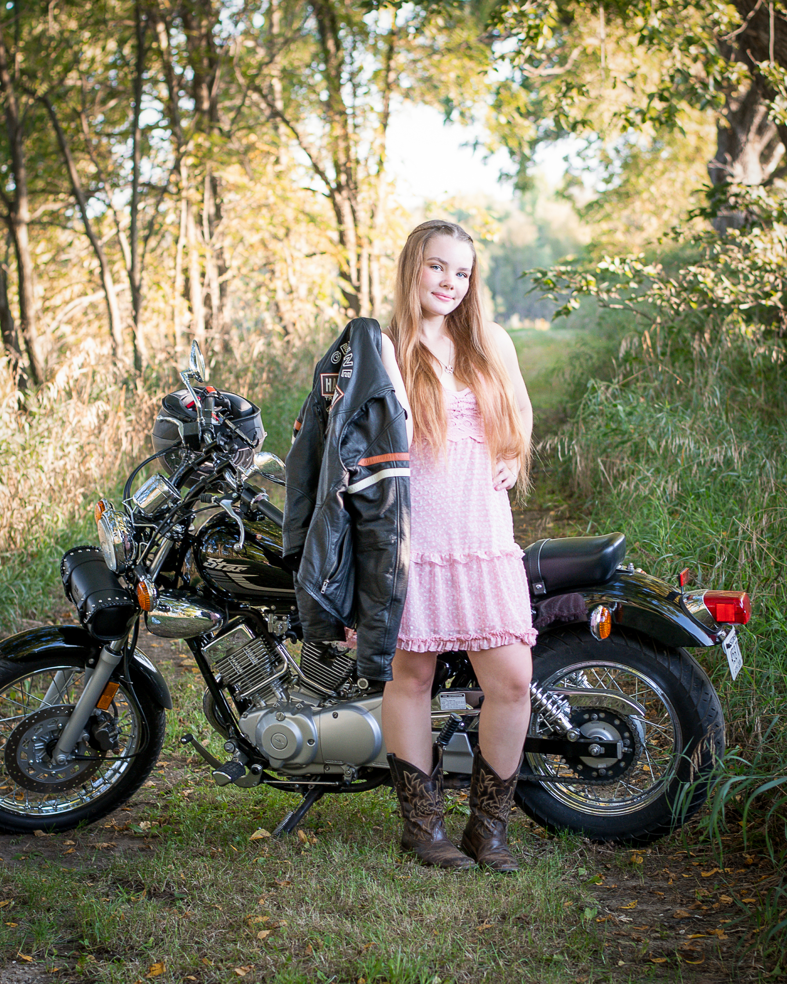 Pretty girl in a pink dress standing in front of her motorcycle in her senior portraits.